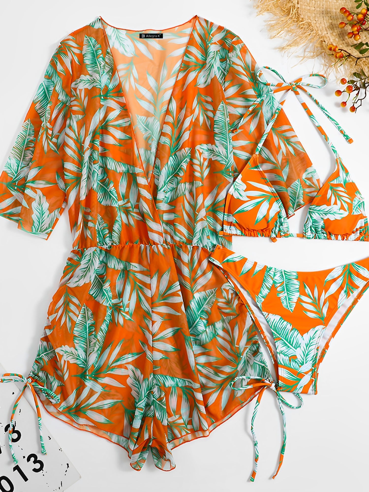 Orange - A woman models a sheer, short-sleeve mini cover-up with a vibrant tropical leaf print in shades of purple, blue, and pink, featuring a deep V-neck, drawstring waist, and ruched sides with ties.
