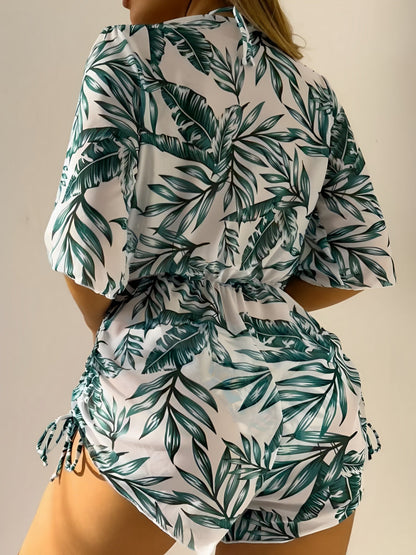 Green - A woman models a sheer, short-sleeve mini cover-up with a vibrant tropical leaf print in shades of purple, blue, and pink, featuring a deep V-neck, drawstring waist, and ruched sides with ties.