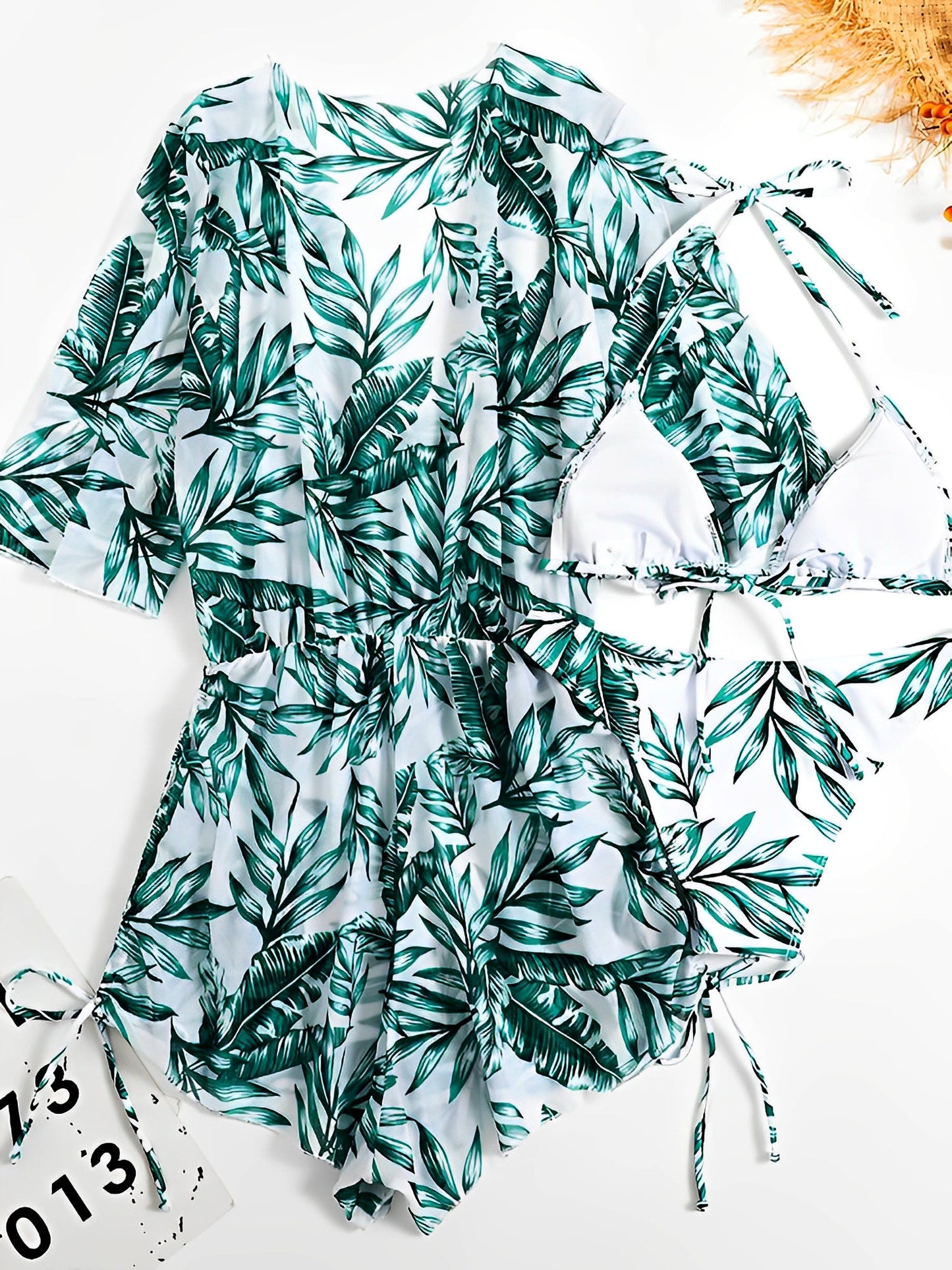 Green - A woman models a sheer, short-sleeve mini cover-up with a vibrant tropical leaf print in shades of purple, blue, and pink, featuring a deep V-neck, drawstring waist, and ruched sides with ties.