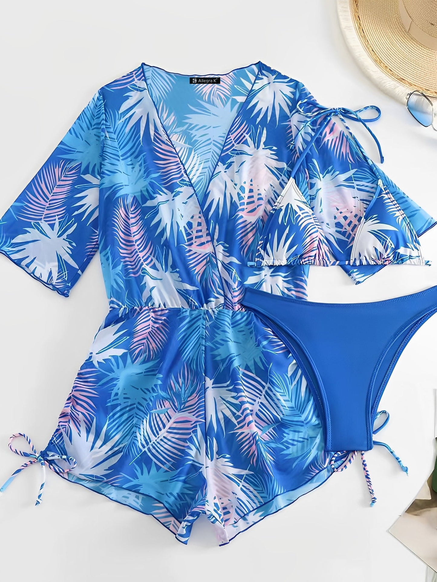 Royal Blue - A woman models a sheer, short-sleeve mini cover-up with a vibrant tropical leaf print in shades of purple, blue, and pink, featuring a deep V-neck, drawstring waist, and ruched sides with ties.