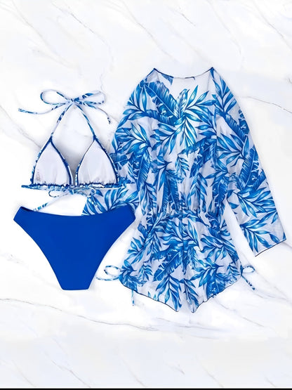 Royal Blue - A woman models a sheer, short-sleeve mini cover-up with a vibrant tropical leaf print in shades of purple, blue, and pink, featuring a deep V-neck, drawstring waist, and ruched sides with ties.