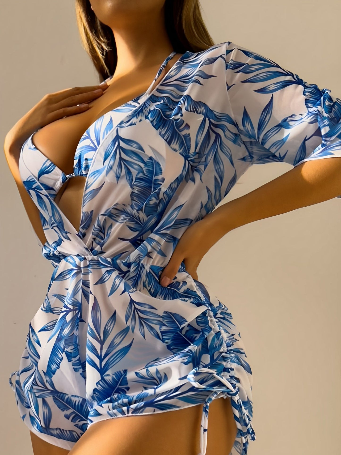 Blue - A woman models a sheer, short-sleeve mini cover-up with a vibrant tropical leaf print in shades of purple, blue, and pink, featuring a deep V-neck, drawstring waist, and ruched sides with ties.