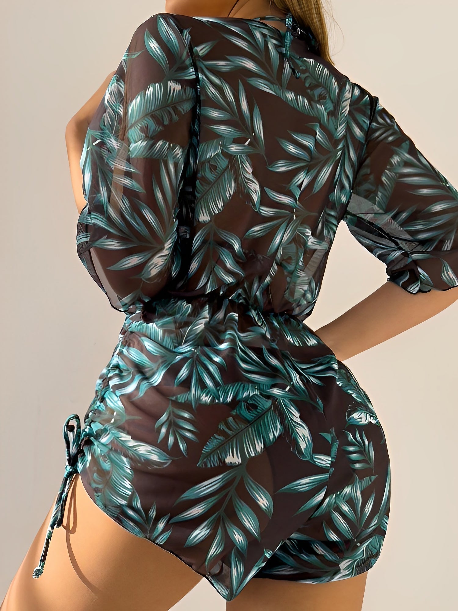 Dark Green - A woman models a sheer, short-sleeve mini cover-up with a vibrant tropical leaf print in shades of purple, blue, and pink, featuring a deep V-neck, drawstring waist, and ruched sides with ties.