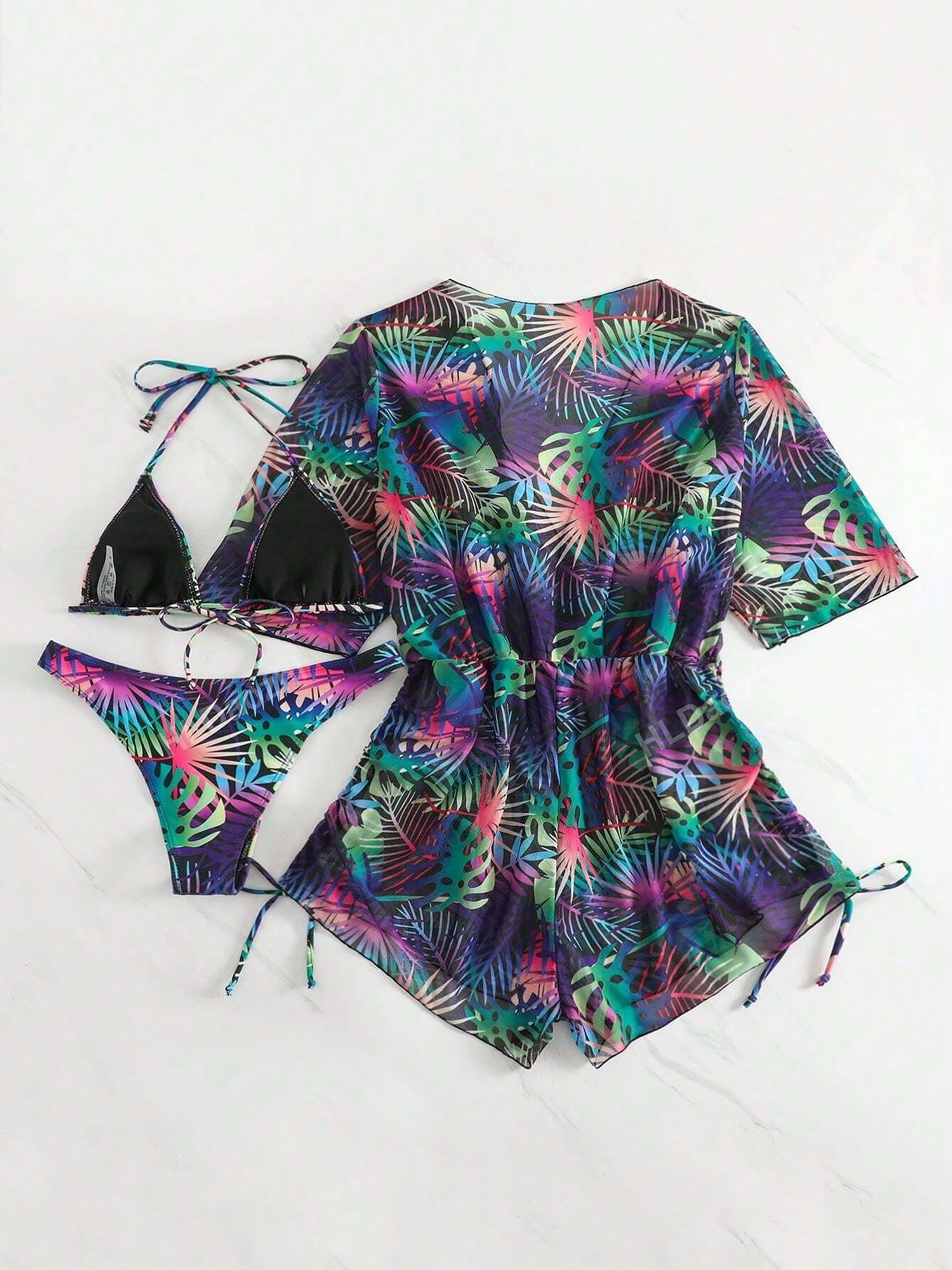 Purple - A woman models a sheer, short-sleeve mini cover-up with a vibrant tropical leaf print in shades of purple, blue, and pink, featuring a deep V-neck, drawstring waist, and ruched sides with ties.