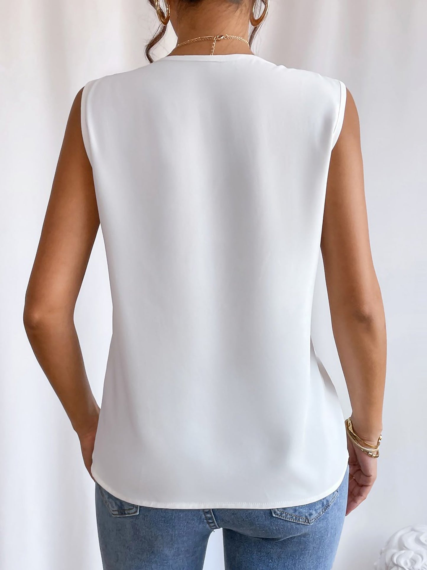 White - Women's solid white sleeveless blouse featuring a deep V-neckline with layered pleat detailing, styled with blue jeans and a black belt.