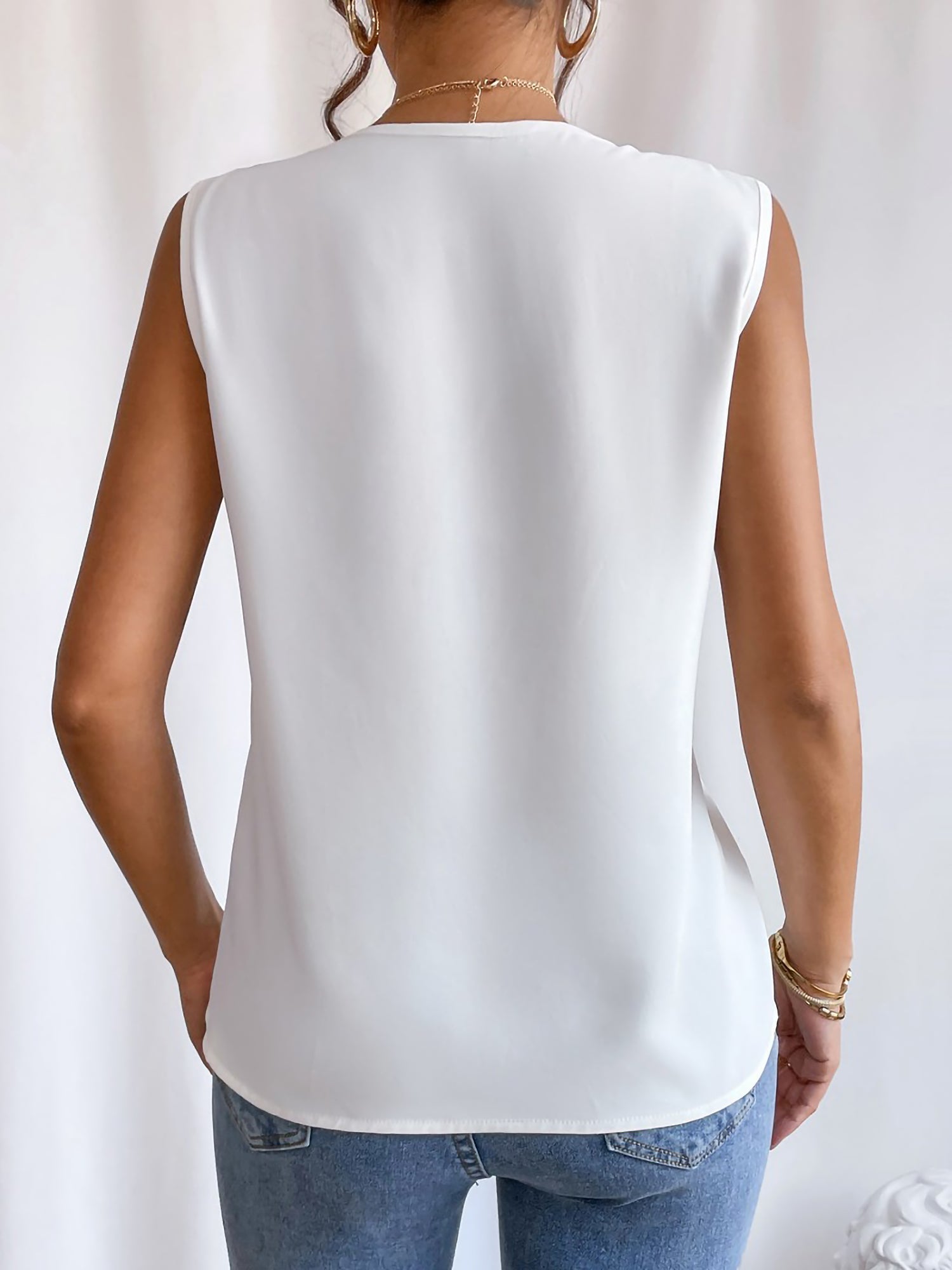 White - Women's solid white sleeveless blouse featuring a deep V-neckline with layered pleat detailing, styled with blue jeans and a black belt.