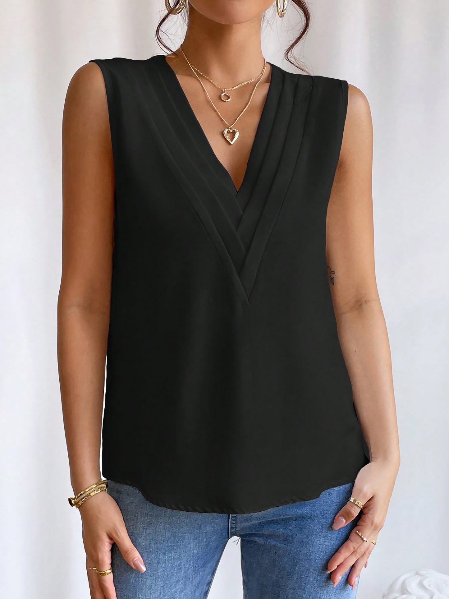 Black - Women's solid white sleeveless blouse featuring a deep V-neckline with layered pleat detailing, styled with blue jeans and a black belt.