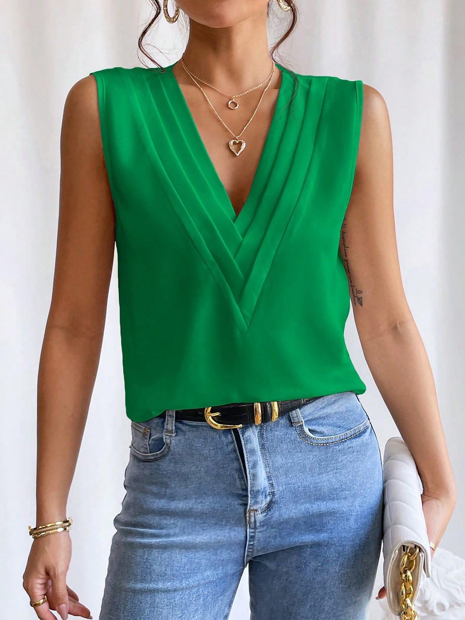 Green - Women's solid white sleeveless blouse featuring a deep V-neckline with layered pleat detailing, styled with blue jeans and a black belt.