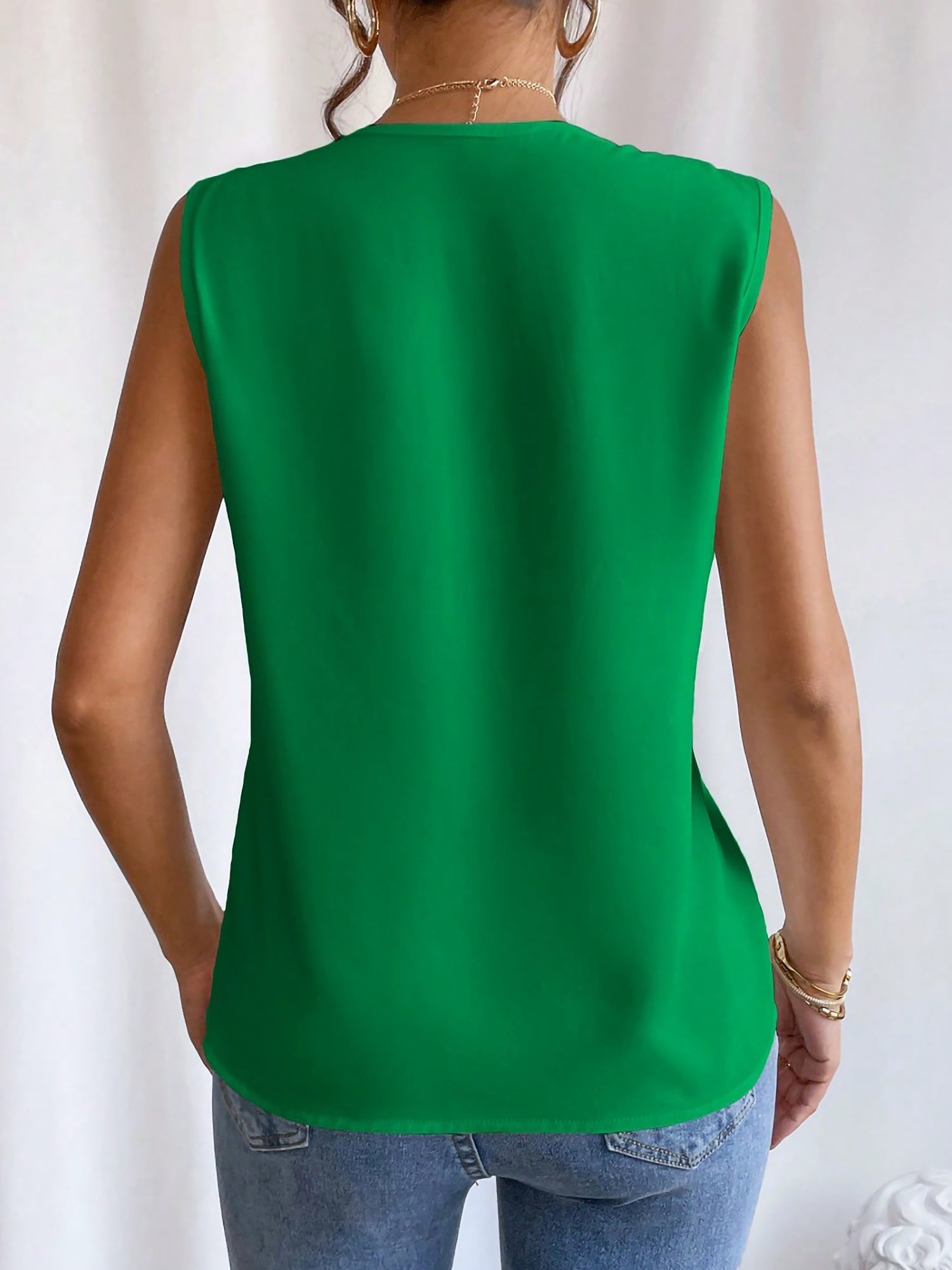 Green - Women's solid white sleeveless blouse featuring a deep V-neckline with layered pleat detailing, styled with blue jeans and a black belt.