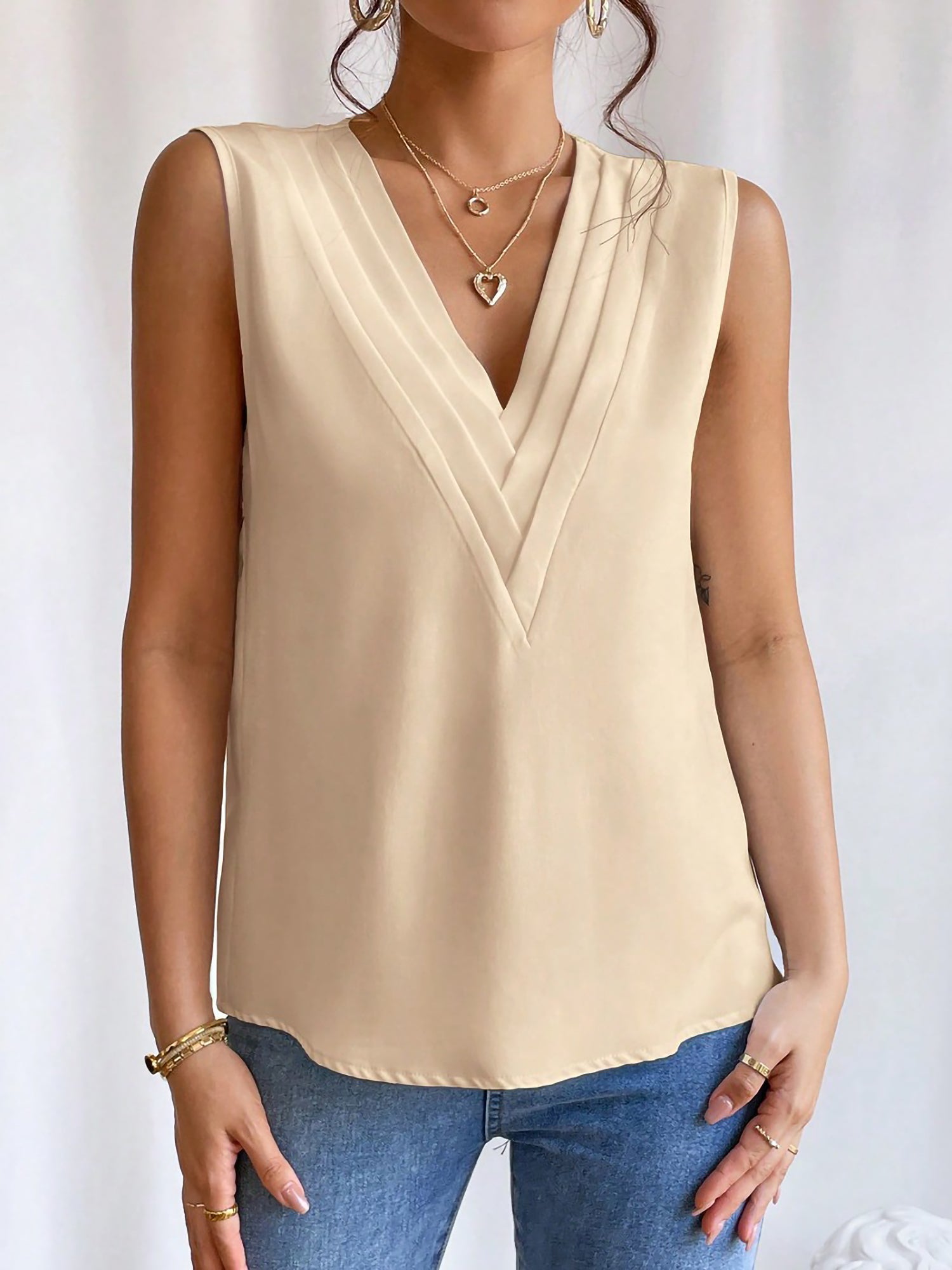 Apricot - Women's solid white sleeveless blouse featuring a deep V-neckline with layered pleat detailing, styled with blue jeans and a black belt.