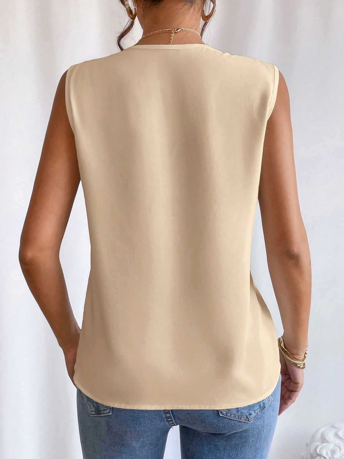 Apricot - Women's solid white sleeveless blouse featuring a deep V-neckline with layered pleat detailing, styled with blue jeans and a black belt.
