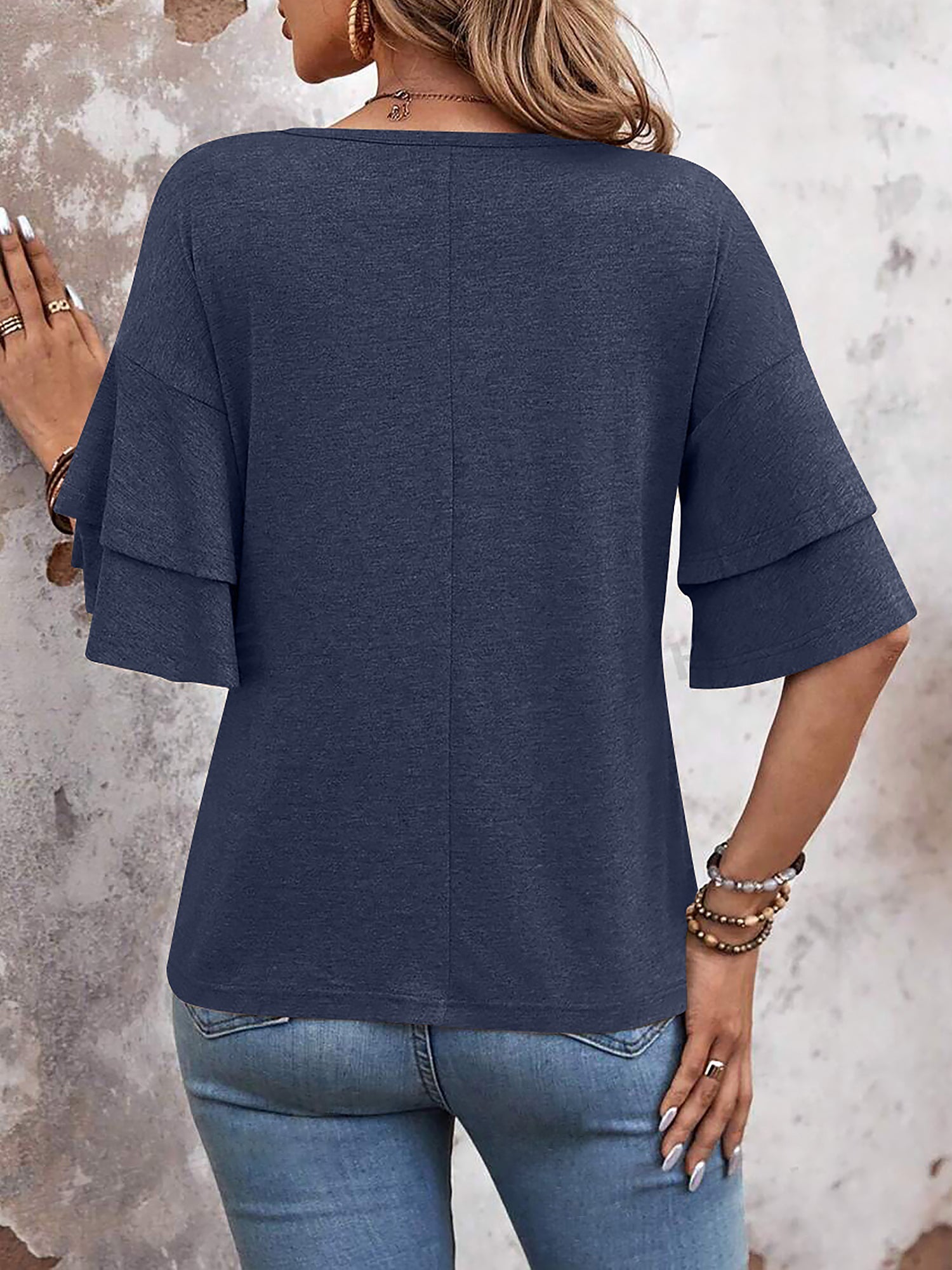 Navy Blue - Women's solid pink V-neck blouse featuring tiered ruffle short sleeves, styled with blue jeans and a long pendant necklace.