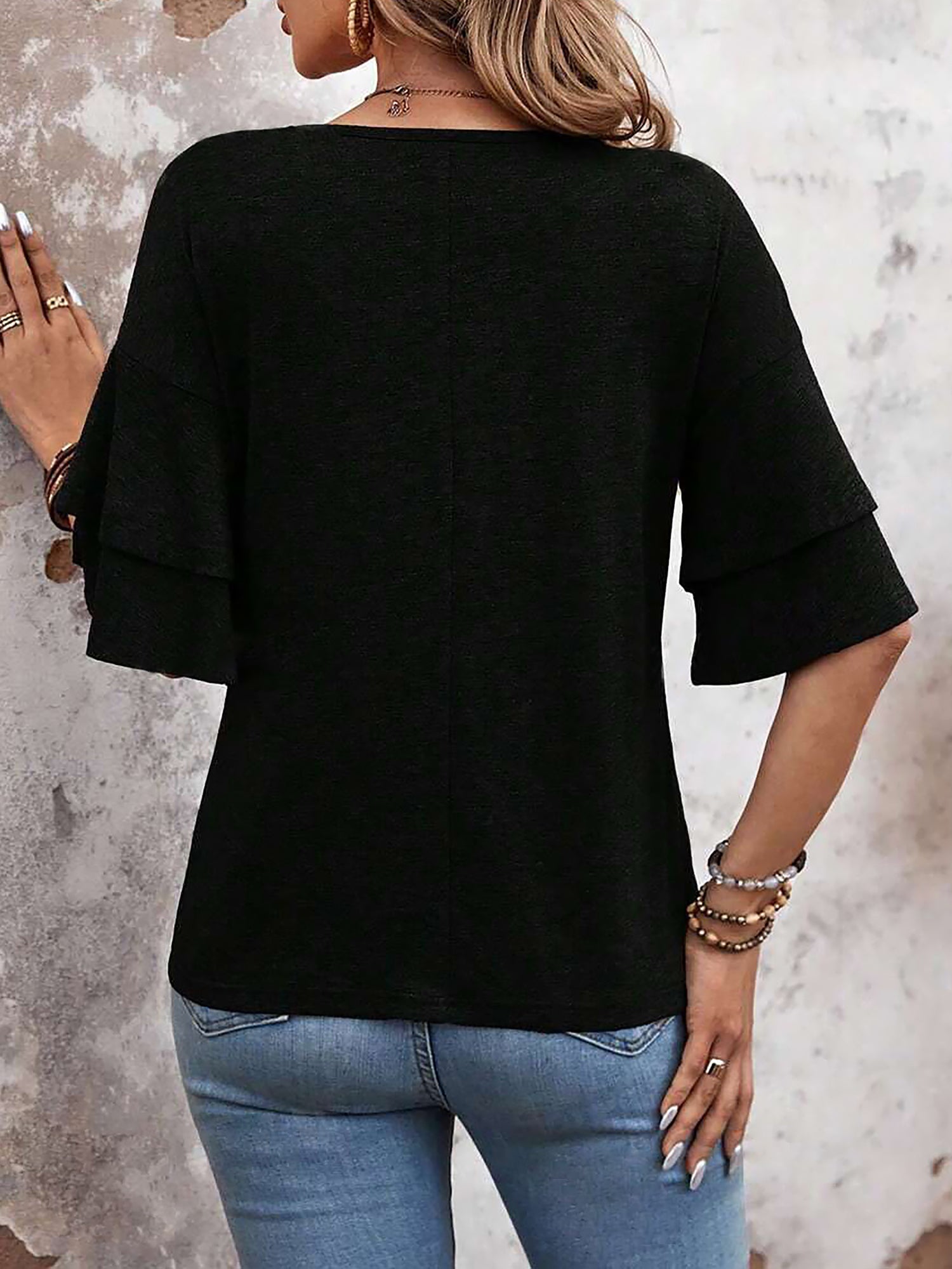 Black - Women's solid pink V-neck blouse featuring tiered ruffle short sleeves, styled with blue jeans and a long pendant necklace.
