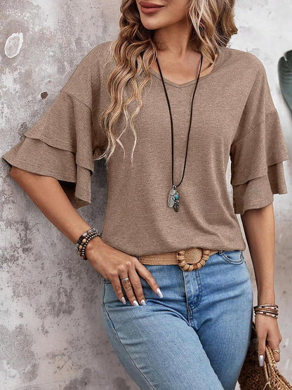 Camel - Women's solid pink V-neck blouse featuring tiered ruffle short sleeves, styled with blue jeans and a long pendant necklace.