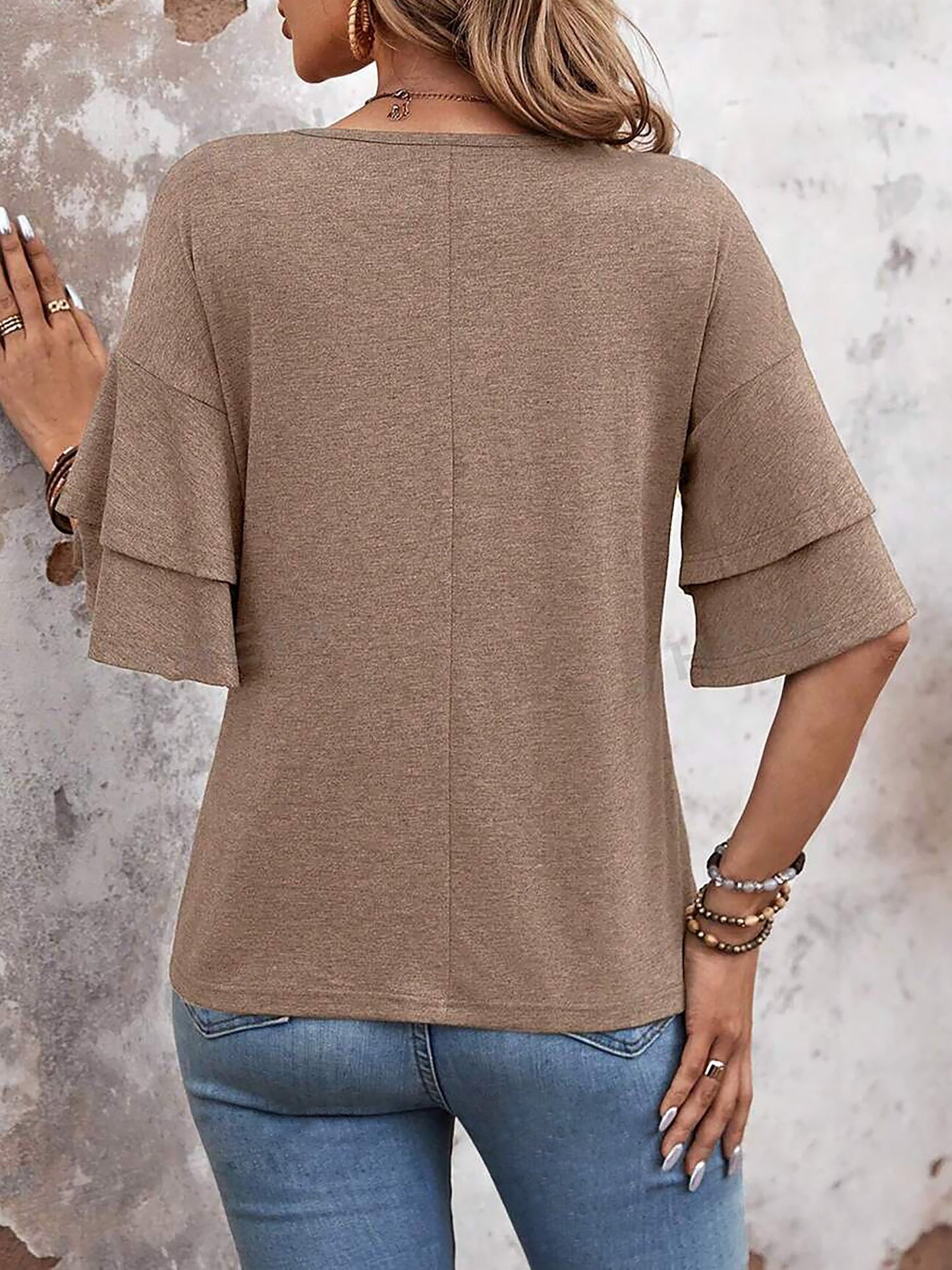Camel - Women's solid pink V-neck blouse featuring tiered ruffle short sleeves, styled with blue jeans and a long pendant necklace.
