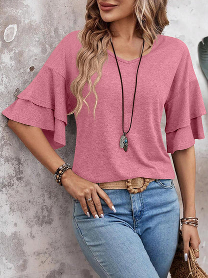 Pink - Women's solid pink V-neck blouse featuring tiered ruffle short sleeves, styled with blue jeans and a long pendant necklace.