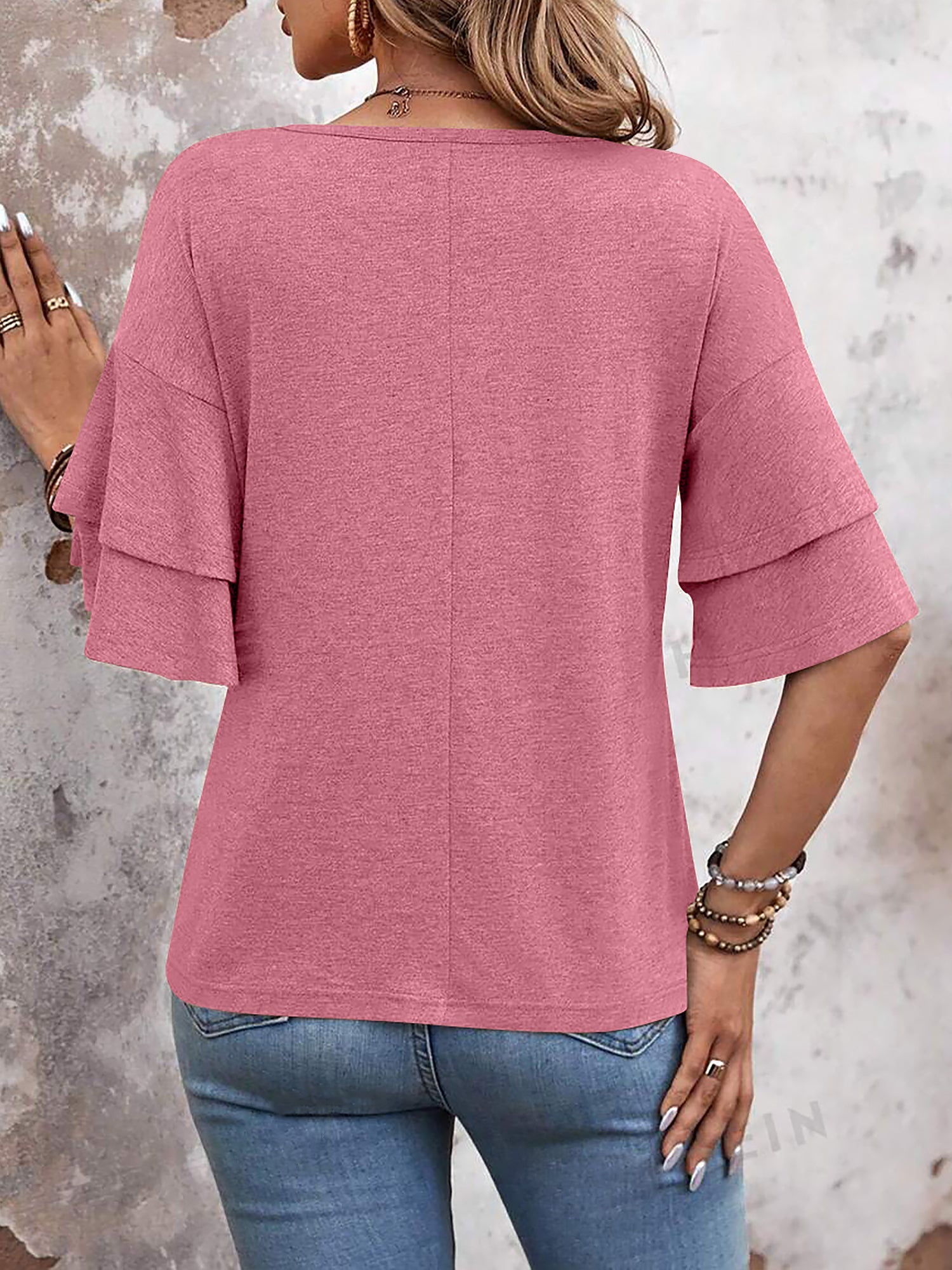 Pink - Women's solid pink V-neck blouse featuring tiered ruffle short sleeves, styled with blue jeans and a long pendant necklace.