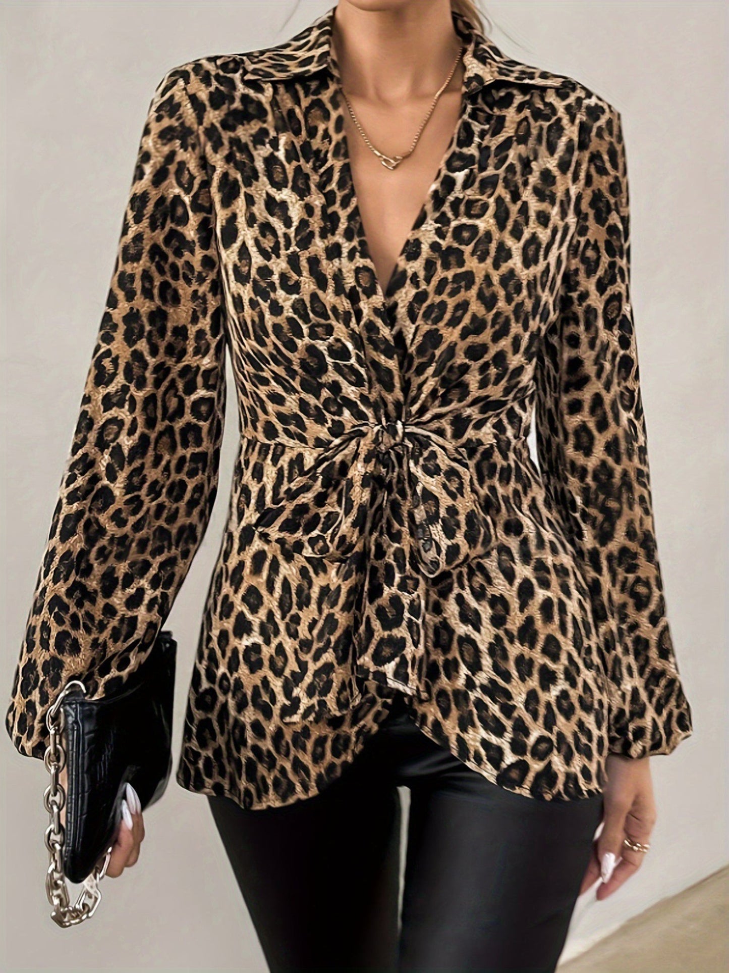 Brown - A woman wearing a long-sleeved, collared, tie-front blouse in a brown and black leopard print, paired with black pants.