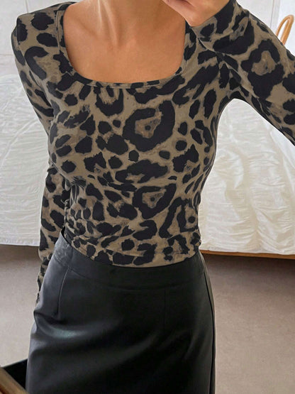 Leopard - A woman seen from the torso up, wearing a form-fitting long-sleeve top with a square neckline and a classic brown and black leopard print, tucked into a black skirt.