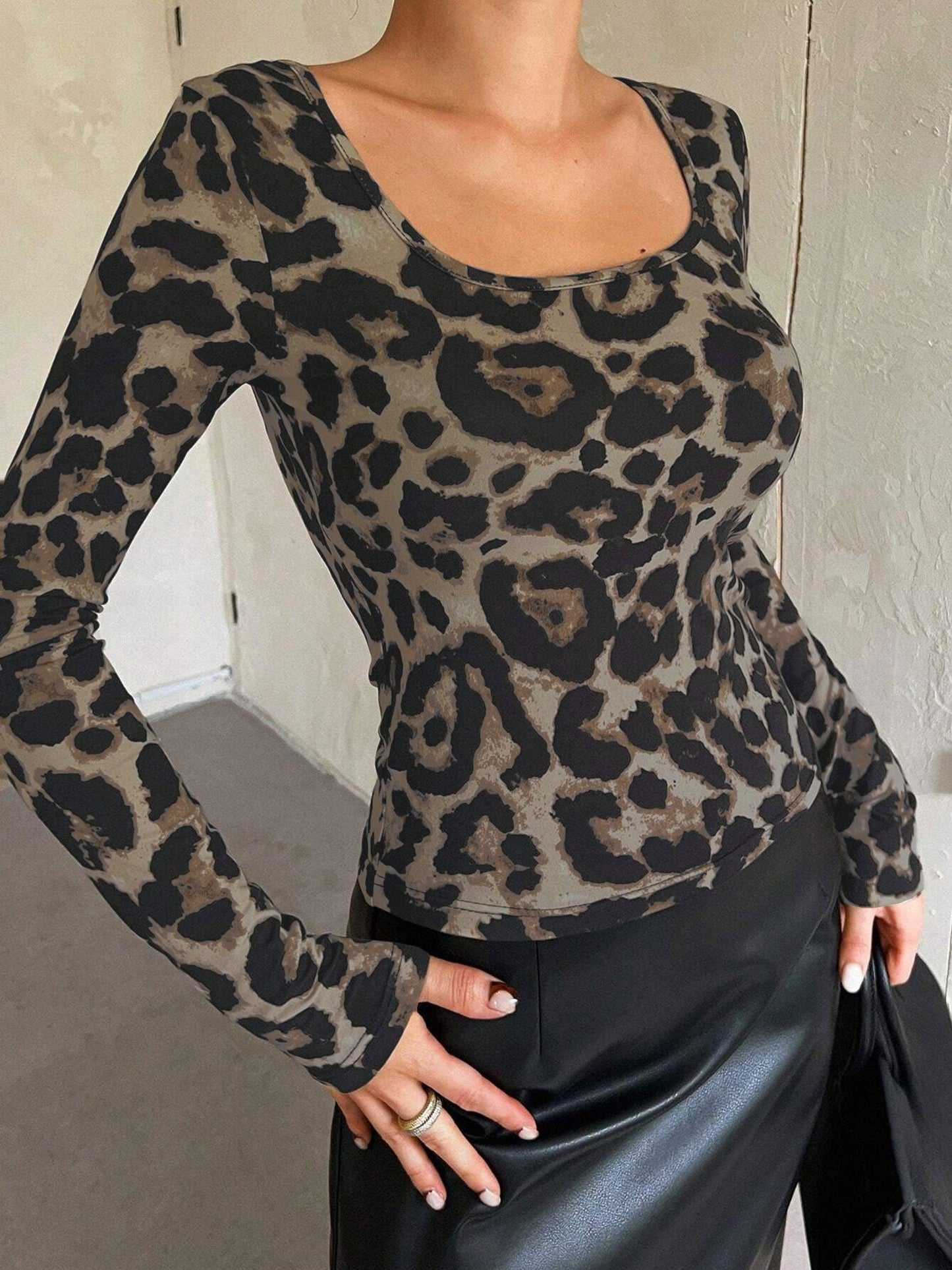 Leopard - A woman seen from the torso up, wearing a form-fitting long-sleeve top with a square neckline and a classic brown and black leopard print, tucked into a black skirt.