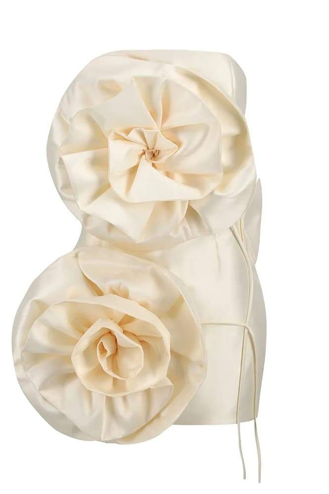 A woman models a strapless, ivory satin mini dress featuring two large, sculptural rosette appliques down the front against a neutral background.