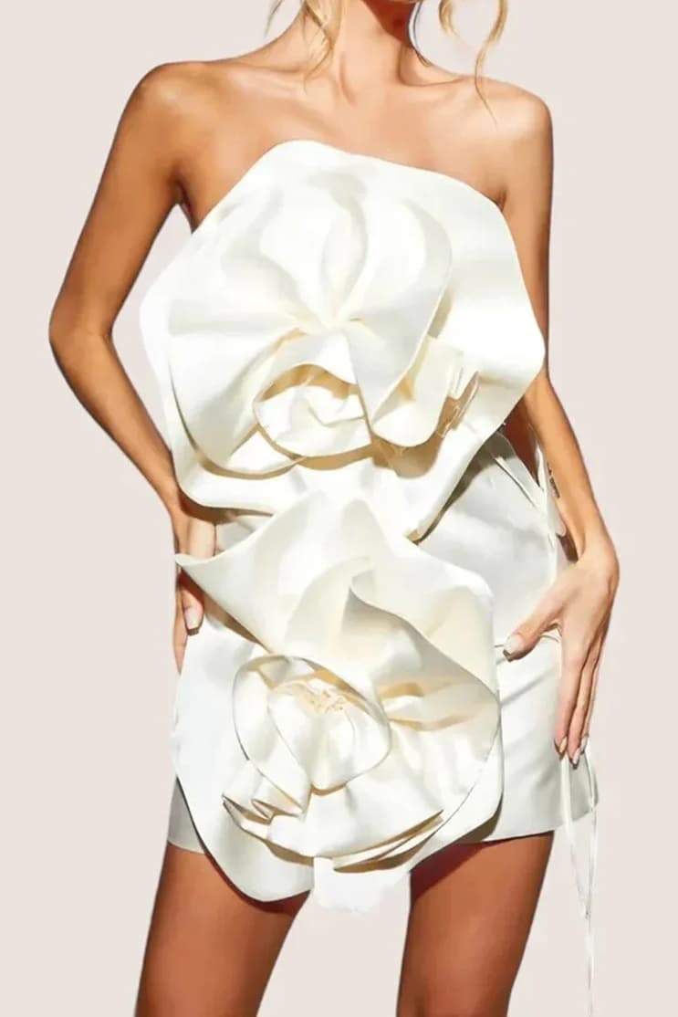 A woman models a strapless, ivory satin mini dress featuring two large, sculptural rosette appliques down the front against a neutral background.