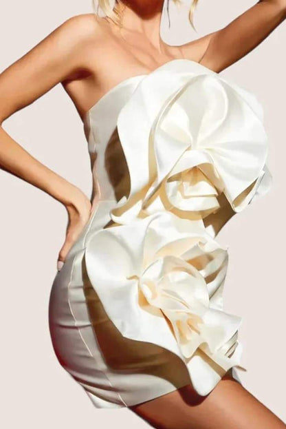 A woman models a strapless, ivory satin mini dress featuring two large, sculptural rosette appliques down the front against a neutral background.
