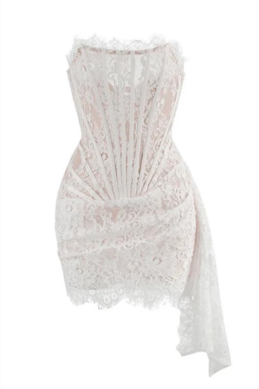 A woman models a white strapless lace mini dress while standing on a grand marble staircase. The dress features a sheer corset bodice with visible boning and a draped, asymmetrical skirt.