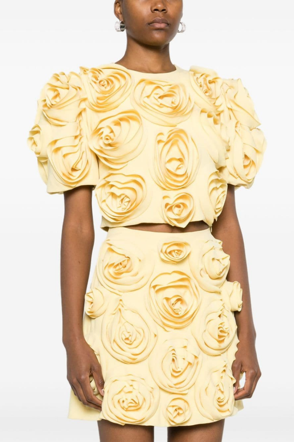 Yellow - A woman wearing a pale yellow two-piece set featuring a cropped top with short puff sleeves and a matching mini skirt, completely covered in large 3D fabric rosette appliqués.