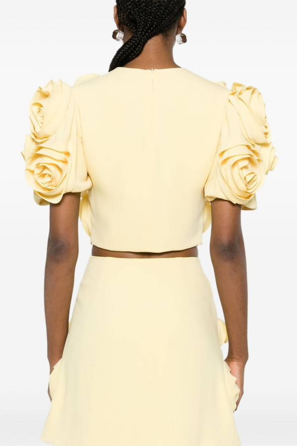 Yellow - A woman wearing a pale yellow two-piece set featuring a cropped top with short puff sleeves and a matching mini skirt, completely covered in large 3D fabric rosette appliqués.