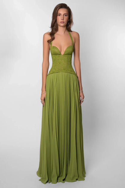 Green - A woman wearing an elegant olive green maxi dress featuring a structured lace corset bodice, halter neckline, and a sweeping floor-length pleated skirt, standing outdoors near stone steps and tropical foliage.