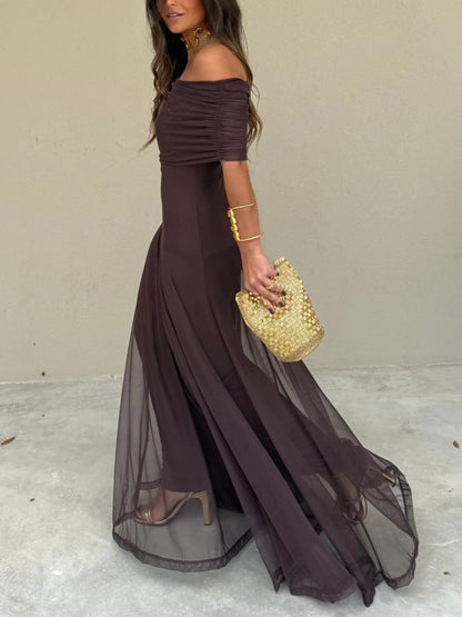 Brown - A woman wearing a dark brown, formal off-the-shoulder maxi dress featuring a ruched neckline and a flowing sheer mesh overlay over a fitted underlay, styled with gold accessories.