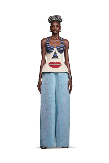 Multi - A woman wearing a structured, cream-colored sleeveless peplum top featuring an avant-garde surrealist face design with striped bust cups and a large red lip motif.