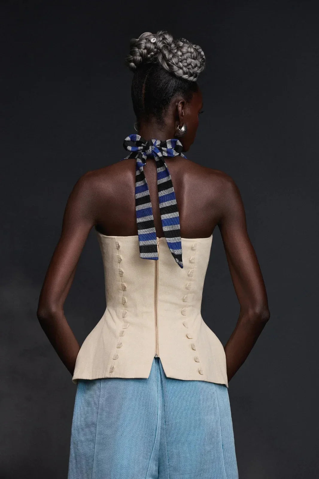 Multi - A woman wearing a structured, cream-colored sleeveless peplum top featuring an avant-garde surrealist face design with striped bust cups and a large red lip motif.