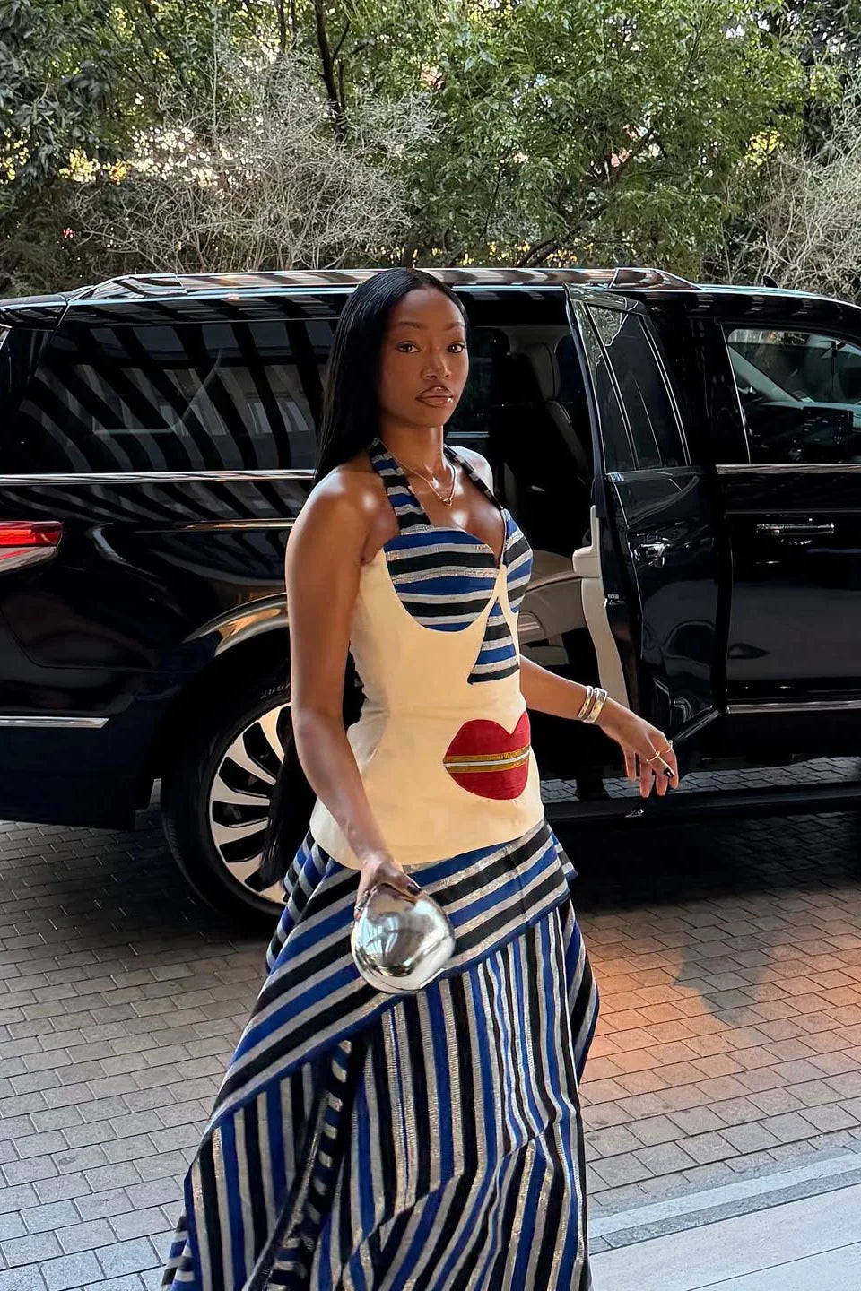 Multi - A woman wearing a structured, cream-colored sleeveless peplum top featuring an avant-garde surrealist face design with striped bust cups and a large red lip motif.