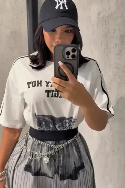 Set - A woman taking a mirror selfie wearing a sheer black vertically pleated maxi skirt layered over light shorts, paired with a graphic t-shirt and chain belt.