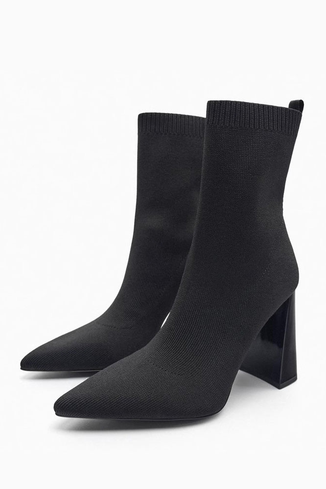 Women's black ribbed knit ankle sock boots featuring a pointed toe and a shiny block heel.