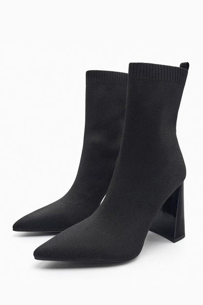 Women's black ribbed knit ankle sock boots featuring a pointed toe and a shiny block heel.