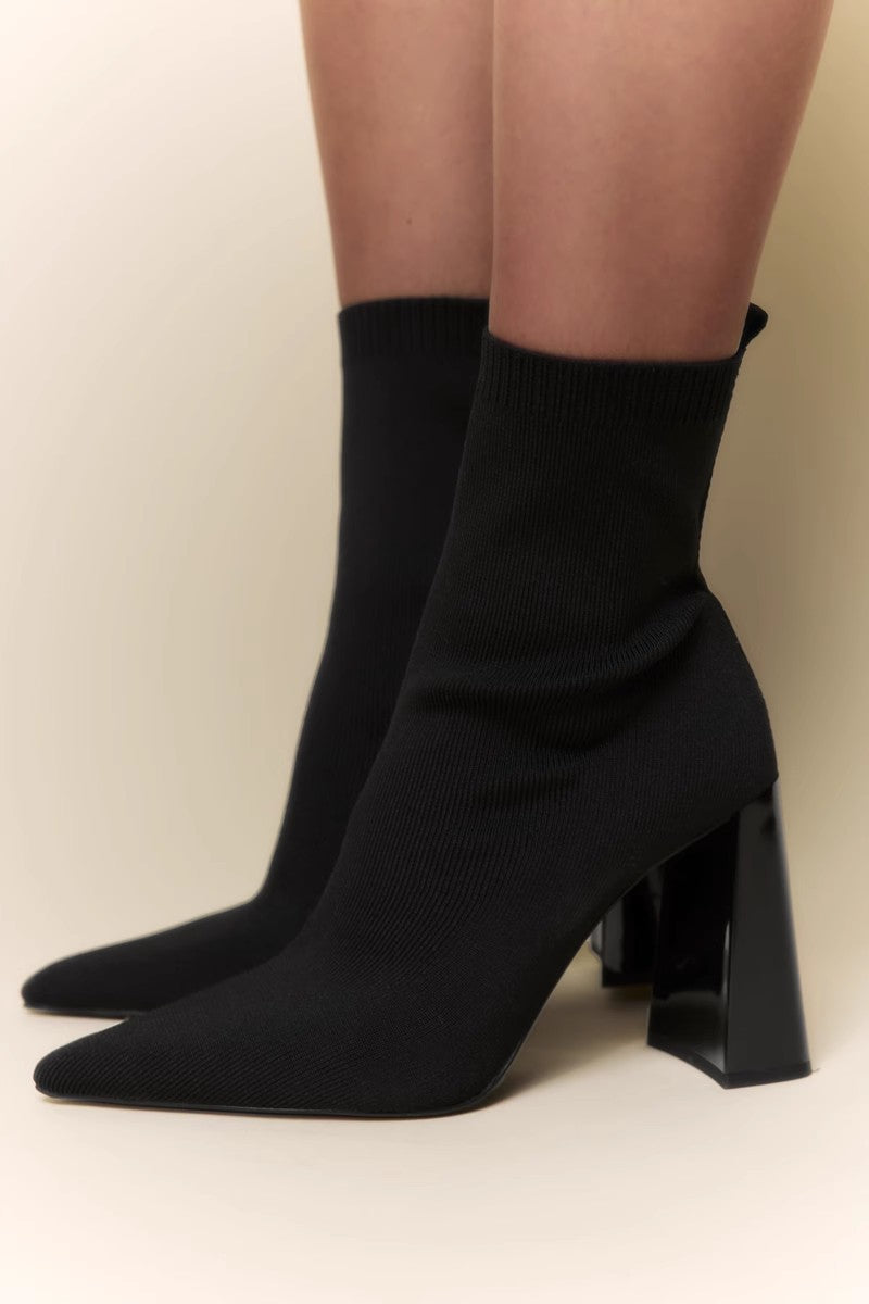 Women's black ribbed knit ankle sock boots featuring a pointed toe and a shiny block heel.
