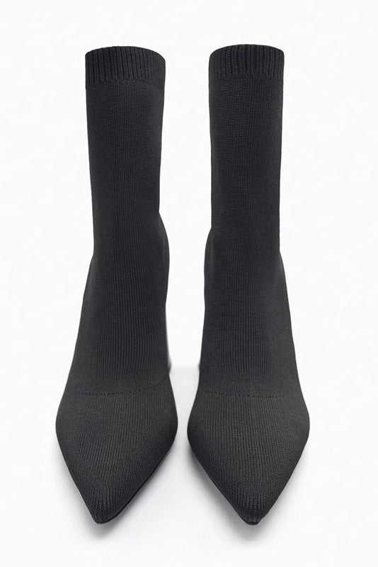 Women's black ribbed knit ankle sock boots featuring a pointed toe and a shiny block heel.