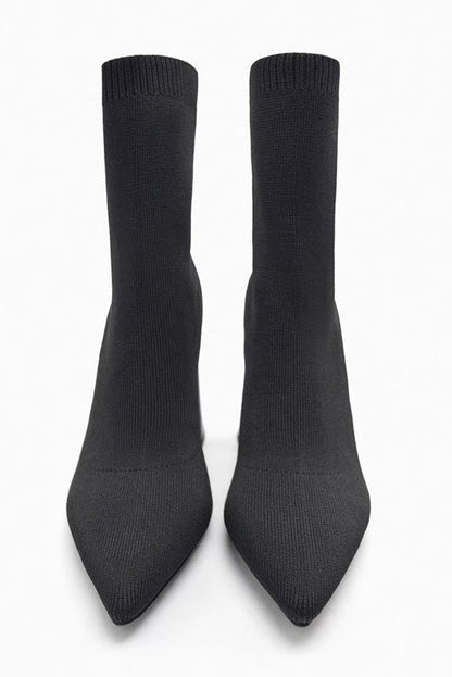 Women's black ribbed knit ankle sock boots featuring a pointed toe and a shiny block heel.