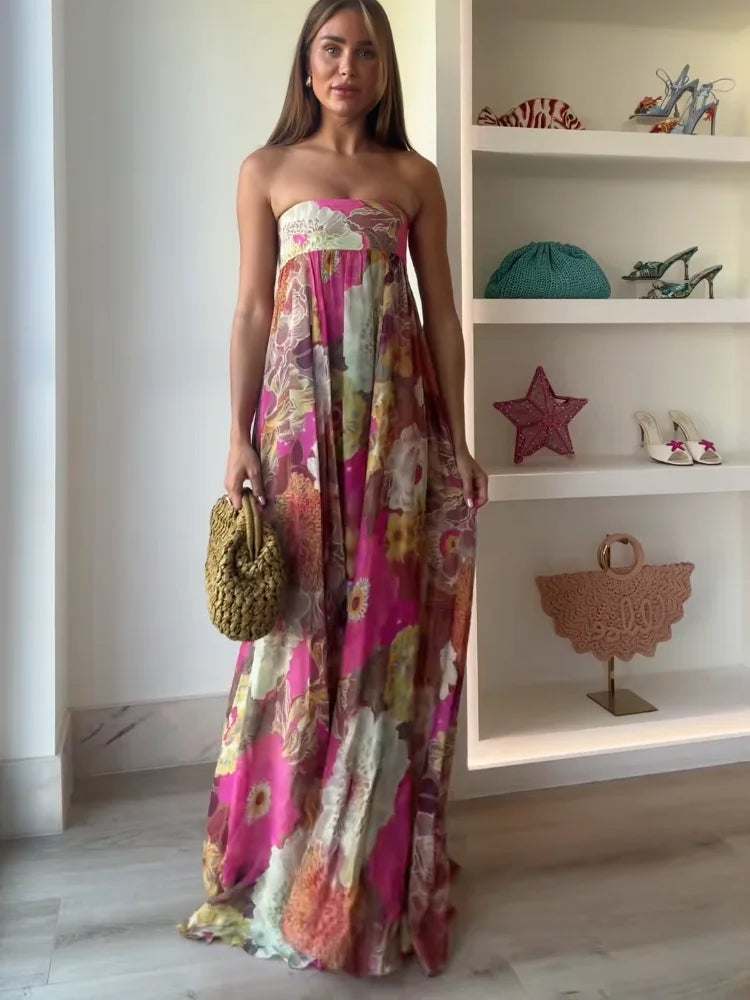 A woman wearing a strapless, flowing maxi dress featuring a vibrant, large-scale floral print in shades of pink, yellow, and green.