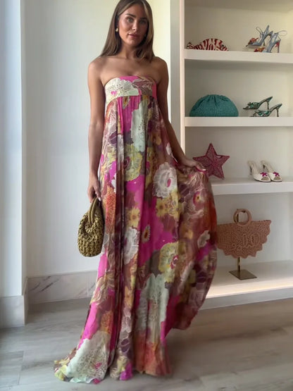 A woman wearing a strapless, flowing maxi dress featuring a vibrant, large-scale floral print in shades of pink, yellow, and green.