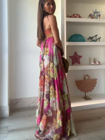 A woman wearing a strapless, flowing maxi dress featuring a vibrant, large-scale floral print in shades of pink, yellow, and green.