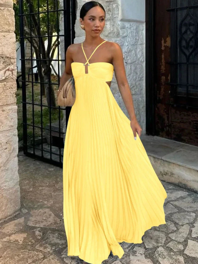 Yellow - A woman walking outdoors wearing a bright yellow, pleated maxi dress featuring a halter neckline, front keyhole, and side cutouts.