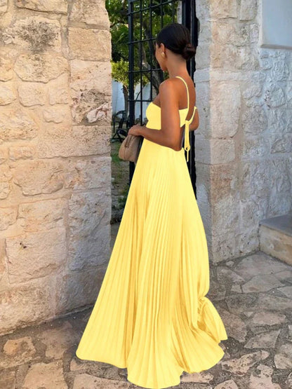 Blue - A woman walking outdoors wearing a bright yellow, pleated maxi dress featuring a halter neckline, front keyhole, and side cutouts.