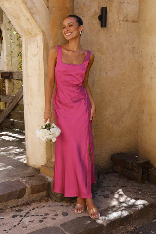 Pink - A woman stands outdoors holding a white bouquet, wearing a bright pink satin midi dress featuring a square neckline, wide straps, and a dramatic high leg slit.