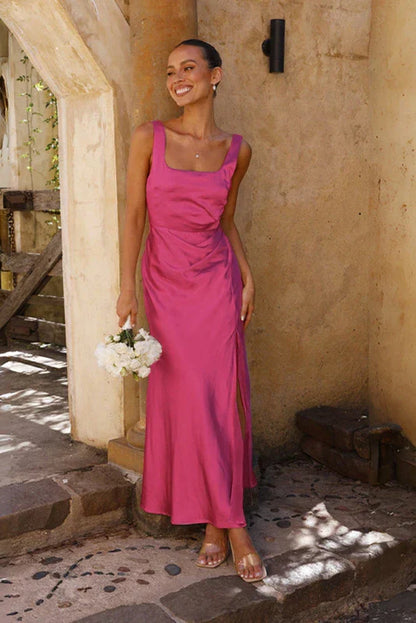 Pink - A woman stands outdoors holding a white bouquet, wearing a bright pink satin midi dress featuring a square neckline, wide straps, and a dramatic high leg slit.