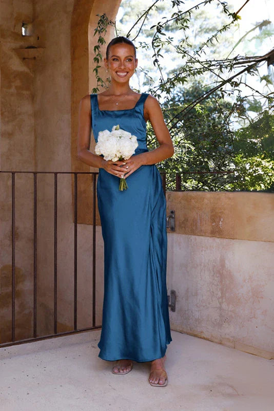 Blue - A woman stands outdoors holding a white bouquet, wearing a bright pink satin midi dress featuring a square neckline, wide straps, and a dramatic high leg slit.