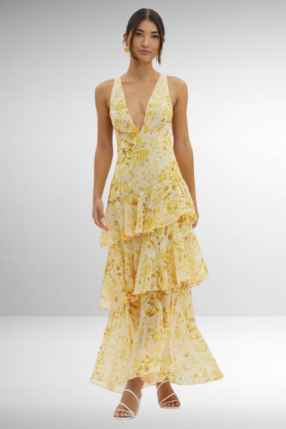 Yellow - A woman wearing a vibrant teal and blue abstract floral print maxi dress featuring a deep V-neckline and a dramatic tiered ruffle skirt.